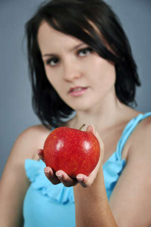 Pretty young woman stretches red apple. 
の写真素材