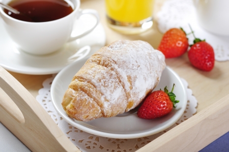 Breakfast with tea and croissants in a wooden tray on tableの写真素材