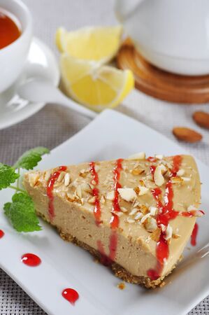 Slice of homemade caramel cheesecake with almond on white plateの写真素材