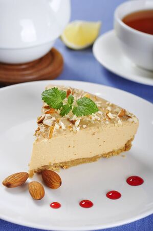 Slice of homemade caramel cheesecake with almond on white plateの写真素材