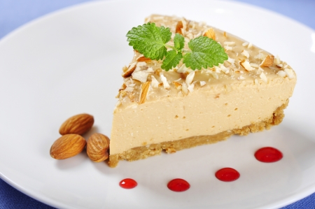 Slice of homemade caramel cheesecake with almond on white plateの写真素材