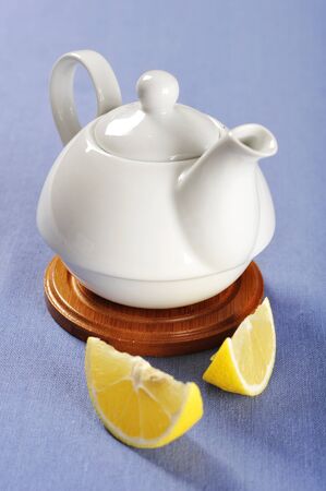 Classic white teapot on a blue tablecloth with slices of lemonの写真素材