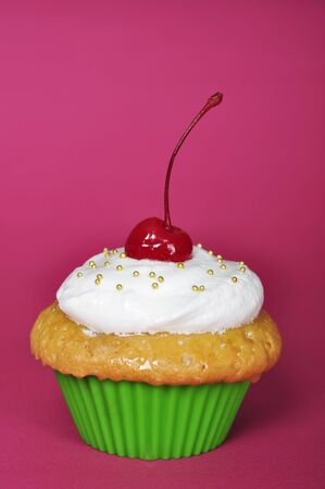 Cupcake with whipped cream and cherry on pink backgroundの写真素材