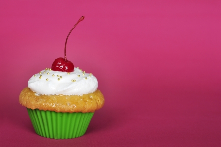 cupcake with whipped cream and cherry on pink backgroundの写真素材