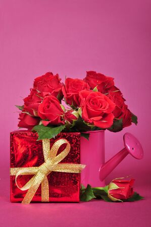 bouquet of red roses in a pink watering can with red gift box on a pink backgroundの写真素材