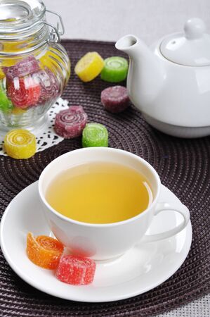 Tea in cup, sweet jelly candies in glass jar and teapotの写真素材