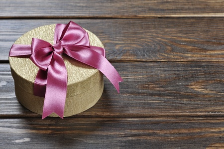 Golden gift box with pink ribbon on wooden backgroundの写真素材