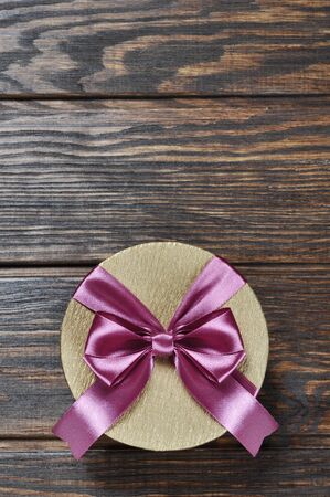 Golden gift box with pink ribbon over wooden backgroundの写真素材