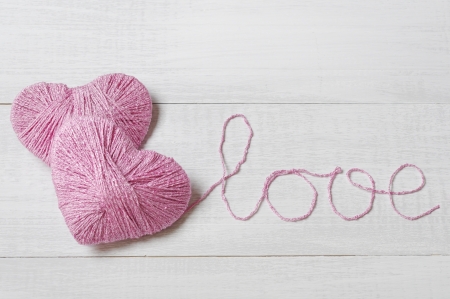 Two pink clews in shape of heart with word   love  made from yarn on  white wooden backgroundの写真素材