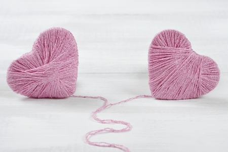Two pink clews in shape of heart on white wooden backgroundの写真素材