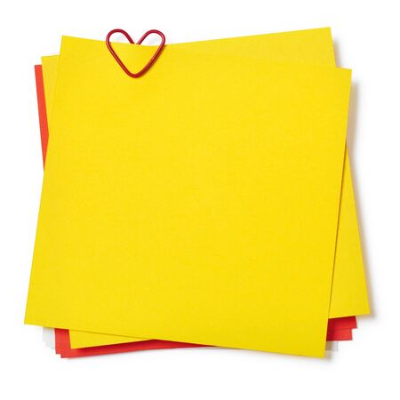 yellow and red sticky notes with paper clip in shape of heart on white backgroundの写真素材