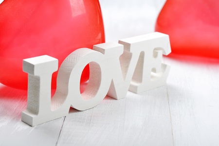 Word "love" made from wood with balloons hearts over white wooden backgroundの写真素材