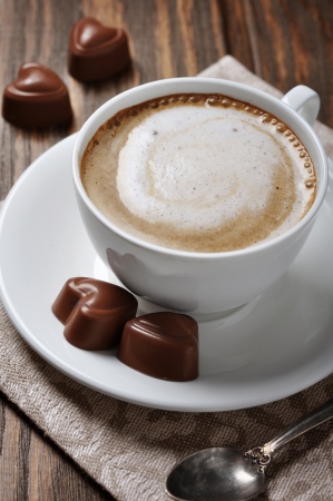 Cup of coffee with chocolate candies over wooden backgroundの写真素材