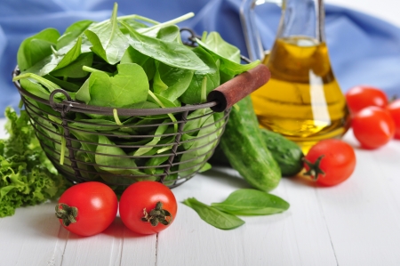 Fresh spinach leaves in basket with tomatoes, cucumber and olive oil on a white wooden backgroundの写真素材