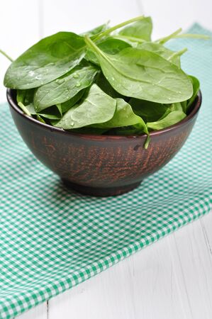 Fresh spinach leaves in brown bowl on a white wooden backgroundの写真素材