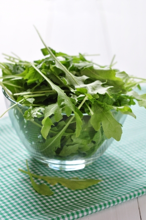 Fresh arugula leaves in glass bowl on a white wooden backgroundの写真素材