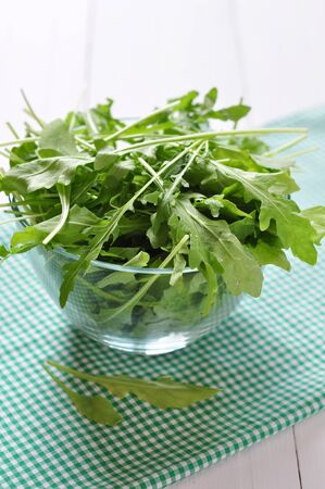 Fresh arugula leaves in glass bowl on a white wooden backgroundの写真素材
