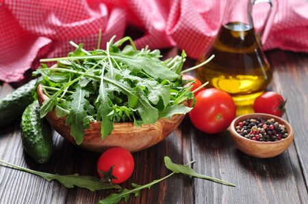 Fresh arugula leaves in wooden bowl with tomatoes, cucumber and olive oil on a wooden backgroundの写真素材