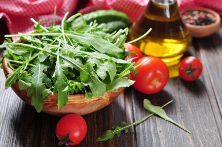 Fresh arugula leaves in wooden bowl with tomatoes, cucumber and olive oil on a wooden backgroundの写真素材