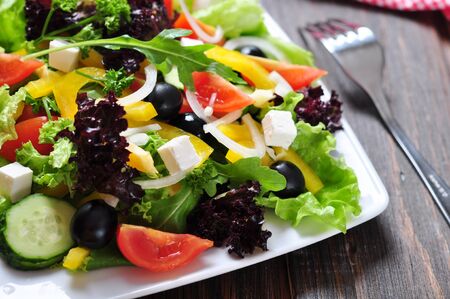 Greek salad on white plate on wooden background closeupの写真素材