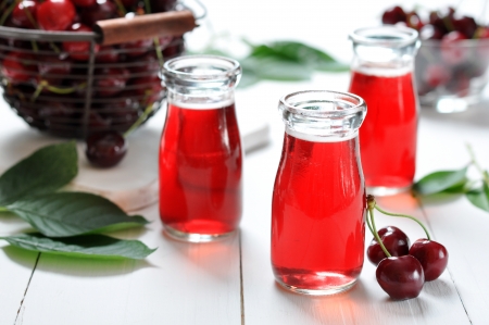 Cherry juice in jars and fresh ripe cherries on wooden backgroundの写真素材