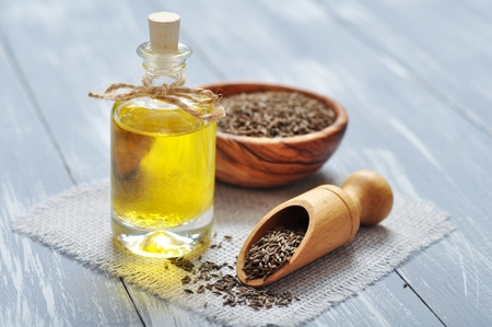 cumin oil in a glass bottle with cumin seeds on wooden backgroundの写真素材
