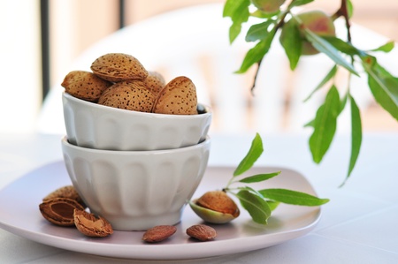 unpeeled almonds nuts in ceramic bowl with  twigs of almond treeの写真素材