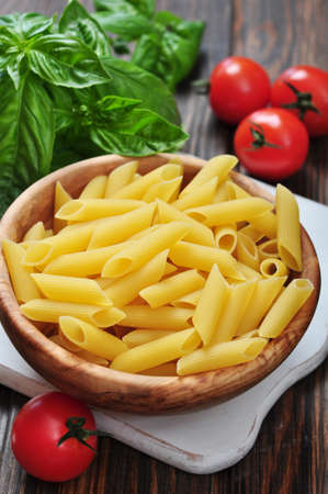 Penne Pasta and tomatoes with basil on wooden cutting boardの写真素材