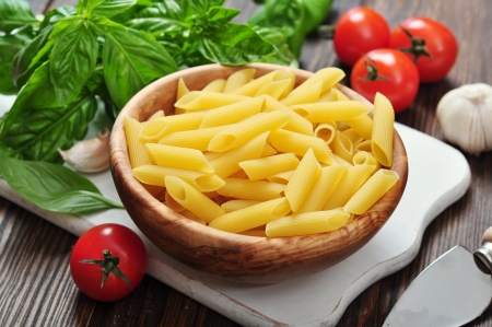 Penne Pasta and tomatoes with basil on wooden cutting boardの写真素材