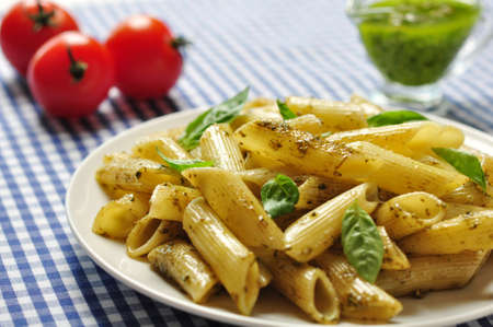 Penne pasta with pesto sauce and basil on white plateの写真素材