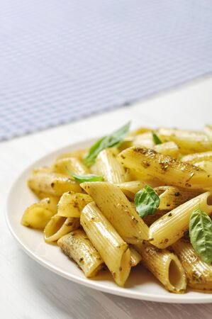 Penne pasta with pesto sauce and basil on white plateの写真素材