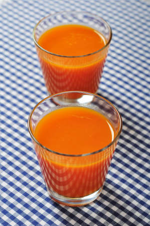 glasses of carrot juice and fresh carrots on checkered backgroundの写真素材