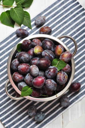 Fresh plums in metal bowl on wooden backgroundの写真素材