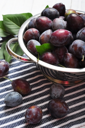 Fresh plum in metal bowl on wooden backgroundの写真素材