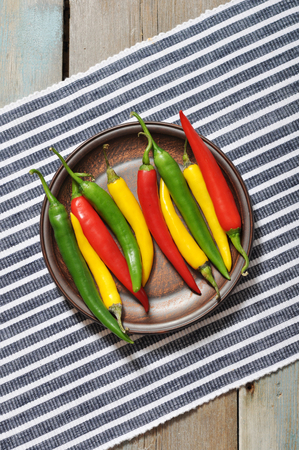 Multi colored hot chili peppers in bowl on vintage wooden backgroundの写真素材