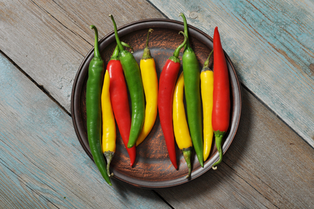Multi colored hot chili peppers in bowl on vintage wooden backgroundの写真素材
