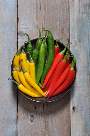Multi colored hot chili peppers in bowl on vintage wooden backgroundの写真素材