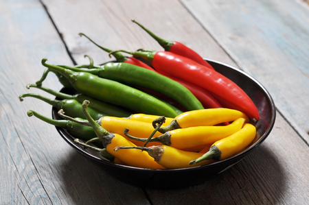Multi colored hot chili peppers in bowl on vintage wooden backgroundの写真素材
