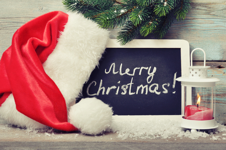 Candle in lantern and framed blackboard with Santa's hat on wooden backgroundの写真素材