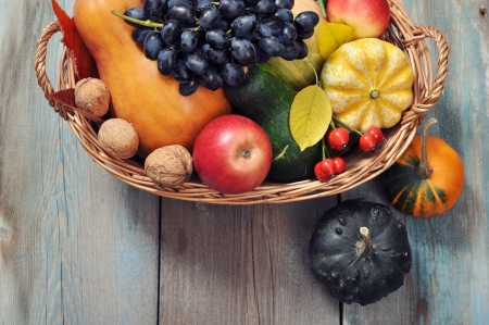 Fresh ripe pumpkins, apples, grape and nuts in wicker basket over wooden backgroundの写真素材