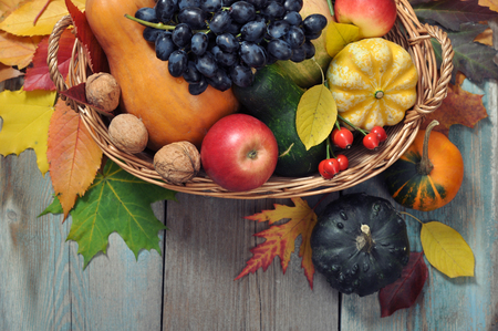 Fresh ripe pumpkins, apples, grape and nuts in wicker basket over wooden background
の写真素材