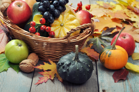 Fresh ripe pumpkins, apples, grape and nuts in wicker basket over wooden backgroundの写真素材