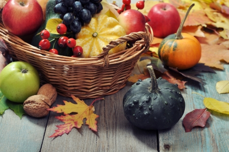 Fresh ripe pumpkins, apples, grape and nuts in wicker basket over wooden backgroundの写真素材
