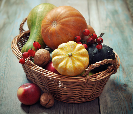 Fresh ripe pumpkins, apples, grape and nuts in wicker basket over wooden backgroundの写真素材