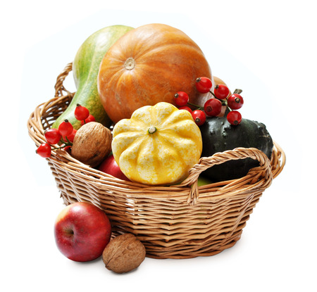 Fresh ripe pumpkins, apples, grape and nuts in wicker basket isolated on whiteの写真素材