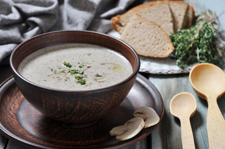 Mushroom cream soup with herbs in brown bowl over wooden backgroundの写真素材