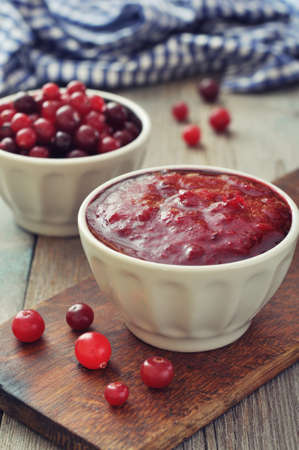 Cranberry sauce in ceramic bowl with fresh berry on wooden backgroundの写真素材