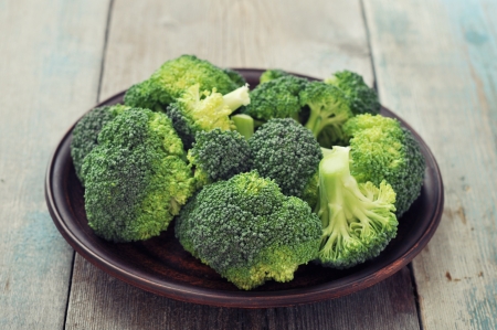 Bunch of fresh green broccoli on brown plate over wooden backgroundの写真素材