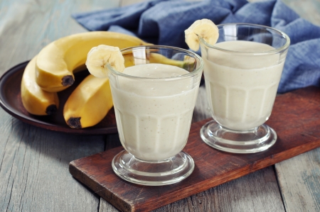 Banana smoothie in glass with fresh fruits on wooden floorの写真素材