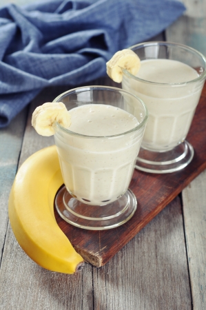 Banana smoothie in glass with fresh fruits on wooden floorの写真素材